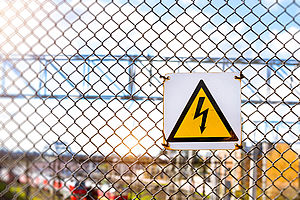 A high voltage warning sign is hanging on a chain-link fence