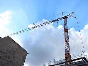A construction crane rises into a blue, slightly cloudy, sky