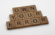 Auf Dem Bild liegen Scrabbelbuchstaben, die den Satz OWN Your Error ergeben.