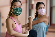 Zwei Sportlerinnen it Maske machen Dehnübungen.